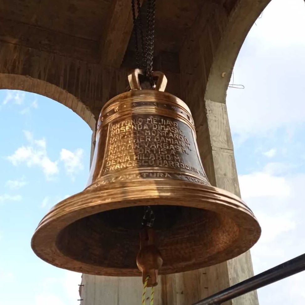 Campana de bronce instalada en una torre, con nombres grabados en su superficie.